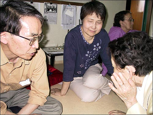 한쪽 귀에 보청기를 댄 이금주 광주유족회장이 가까이 소리를 듣기 위해 귀를 기울이고 있다. 왼쪽은 하나부사 도시오(花房俊雄) 지원단 사무국장. 가운데는 그 부인. 